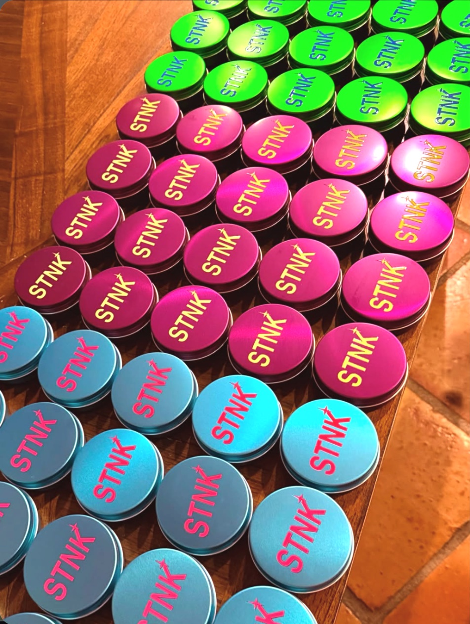 Rows of STNK tins in magenta, lime and teal on a wooden table